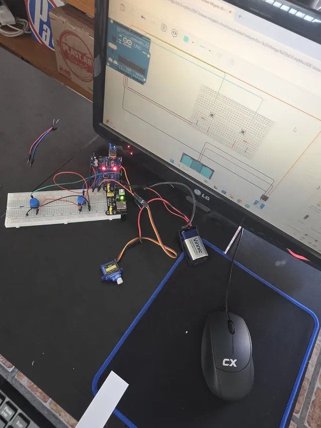 Placa Arduino con protoboard y servomotor conectados frente a un monitor con el circuito simulado.